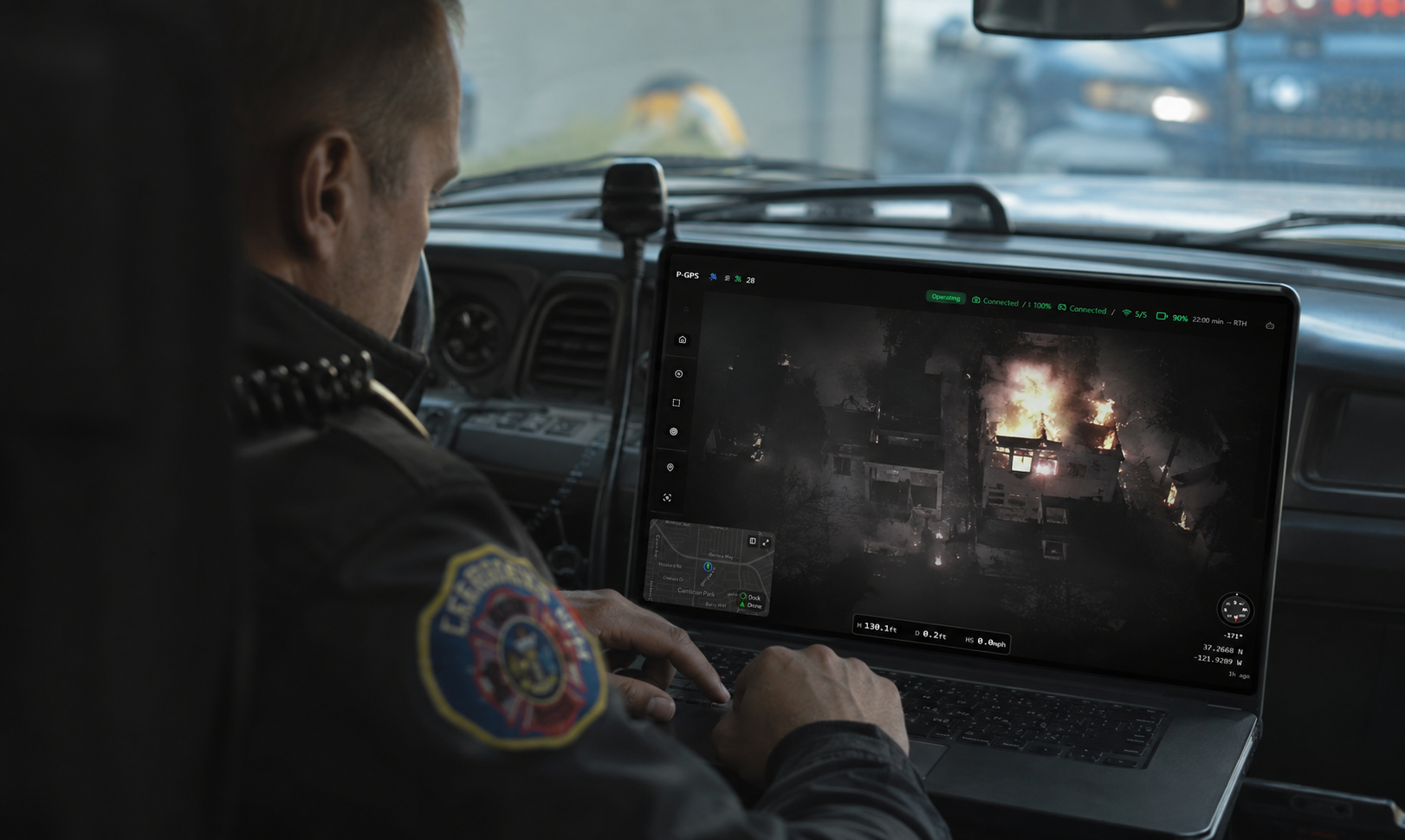 Firefighter reviewing a live drone feed of an active fire from a laptop inside the fire truck cab