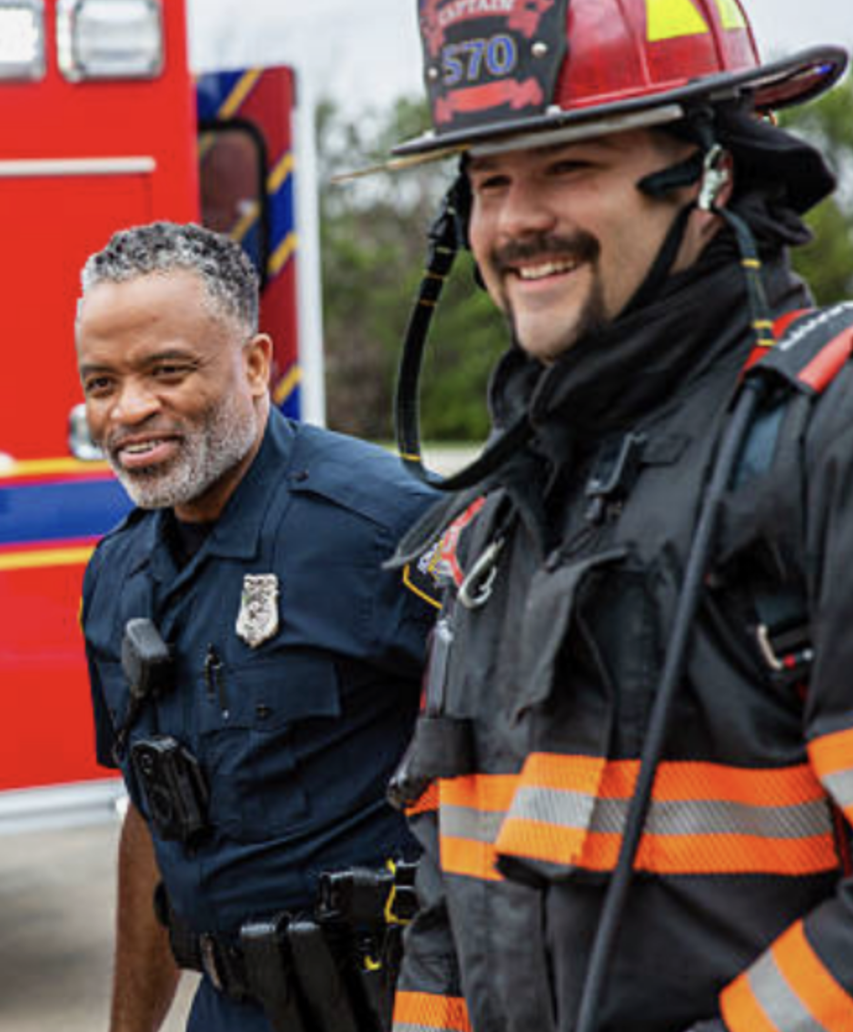 Police officer and firefighter standing side by side, smiling after a call